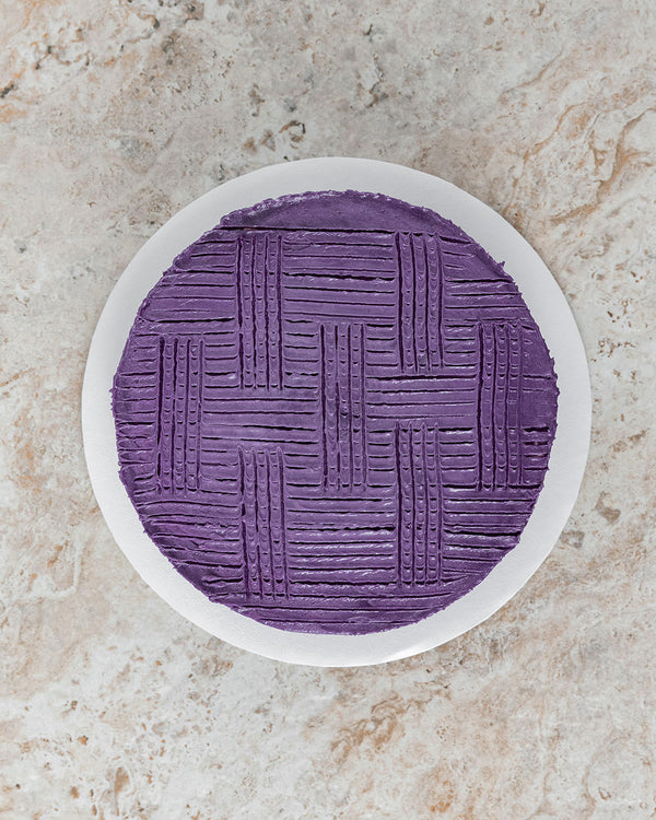 Aerial image of a Ube San Rival round cake, frosted with Ube buttercream and vertical and horizontal streaks for decoration.