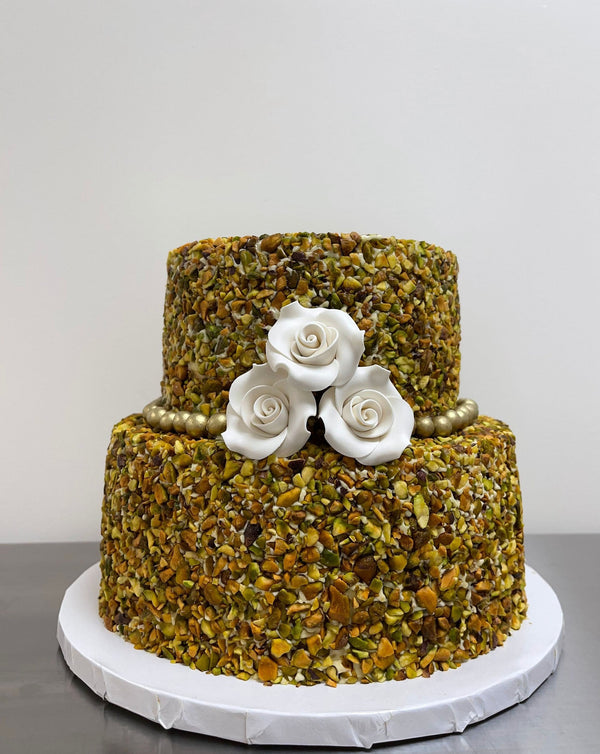 A Two-Tier Pistachio San Rival cake, covered in pistachio nuts and decorated with three frosted white roses, gold beading.