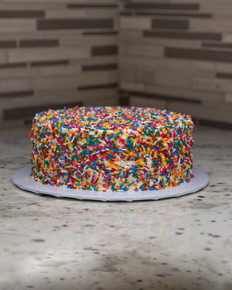 Side image of a Birthday San Rival Cake, covered in buttercream multicolor sprinkle frost. 