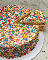 Birthday San Rival Cake slice of cake, showing three layers of cashew meringue, dressed in birthday cake buttercream covered in sprinkles.