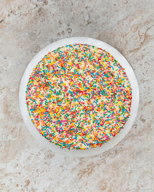 Aerial image of a Birthday San Rival round cake covered in buttercream multicolor sprinkle frost. 