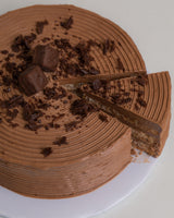 Angled image of a Chocolate San Rival slice, showing a 3 layers of cashew meringue, dressed in chocolate buttercream topped with snickers and chocolate chips.