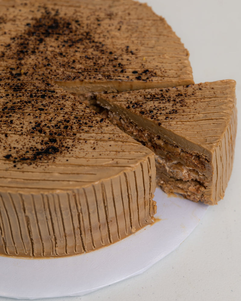 Angled image of a Coffee San Rival slice of cake, showing 3 layers of cashew meringue, dressed in coffee buttercream.