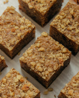 Five golden "Food For The Gods" bars. The bars are topped covered with different kinds of nuts.