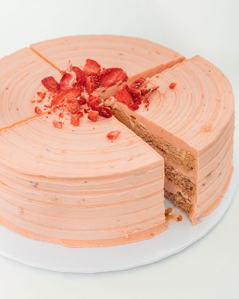 Four perfectly cut slices of a pink Strawberry San Rival sound cake. One slice is displaying three layers of cashew meringue, dressed in strawberry buttercream and topped with freeze-dried strawberries.