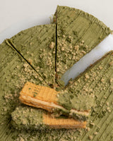 Close-up shot of a green Matcha San Rival round cake, with two slices cut, topped with two vanilla wafers and crushed graham. 