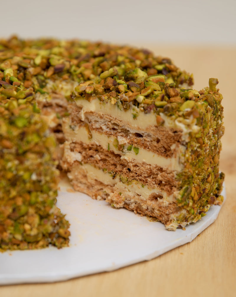 Pistachio San Rival slice of cake, showing three layers of cashew meringue and buttercream, covered with pistachio nuts.