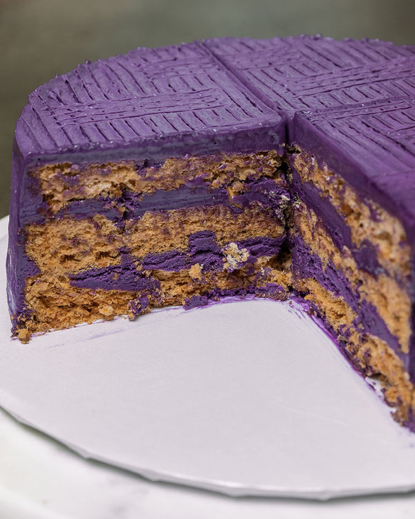Three-fourths of a Ube San Rival round cake, displaying its three layers of cashew meringue, dressed in Ube buttercream
