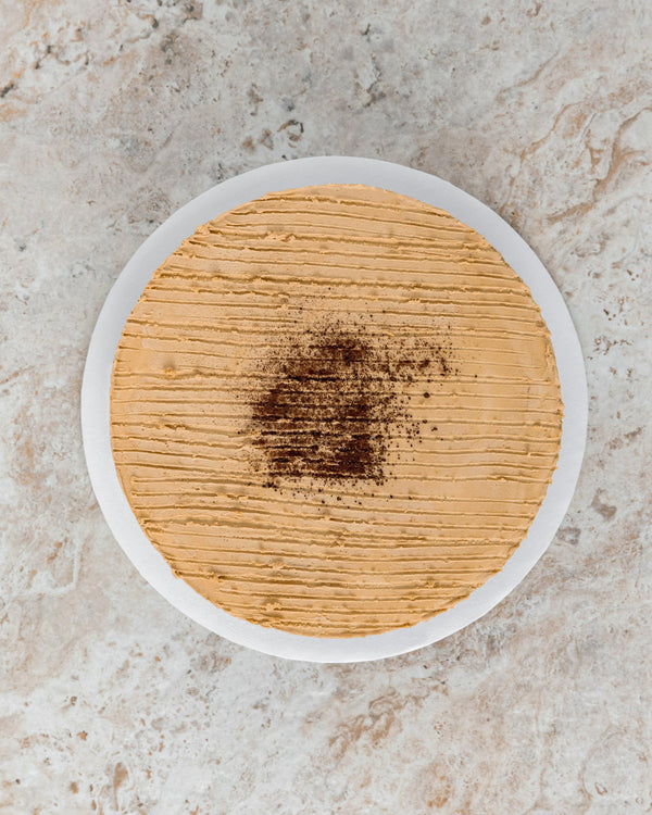 Aerial image of a Coffee San Rival round cake, frosted in coffee buttercream with vertical lines across, and grounded coffee sprinkled on top.