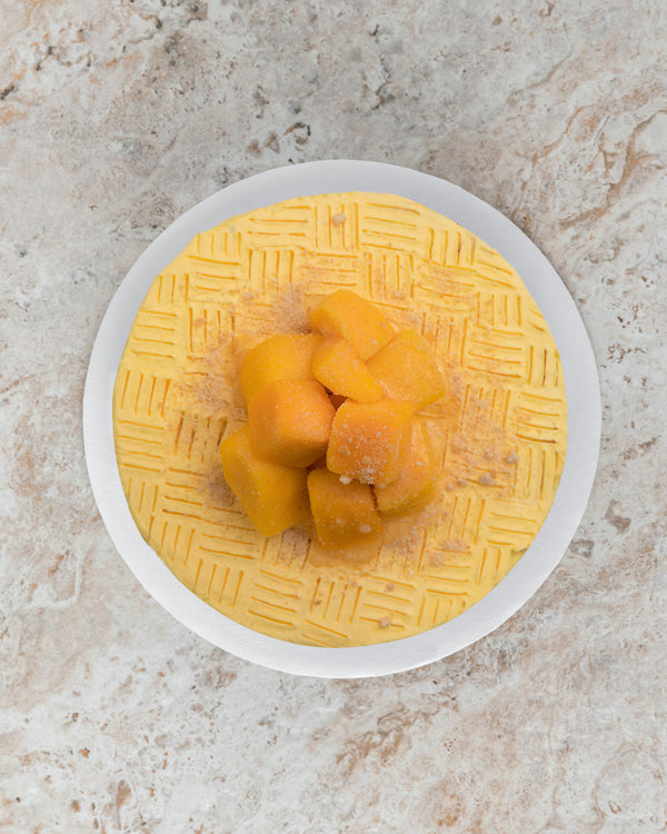 Aerial image of a yellow Mango San Rival round cake, frosted with mango buttercream, topped with frozen mango and crushed graham. 