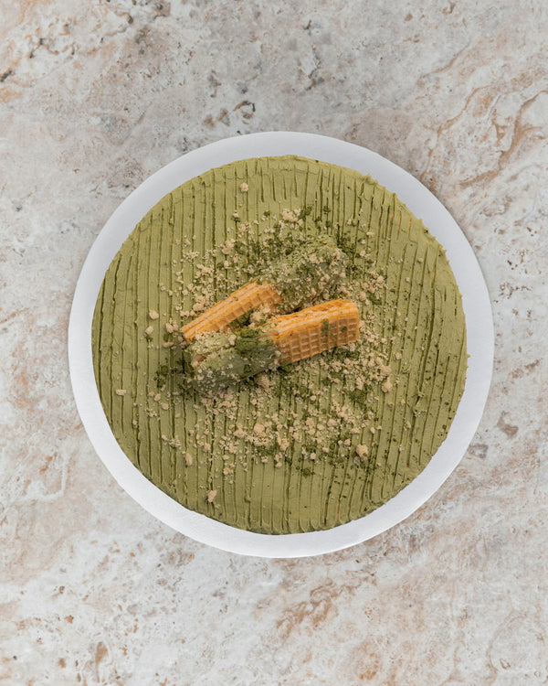 Aerial image of a green Matcha San Rival round cake, frosted with matcha buttercream topped with two vanilla wafers and crushed graham. 