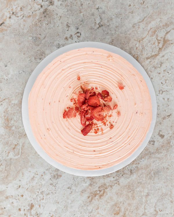Aerial image of a pink Strawberry San Rival round cake, frosted in strawberry buttercream and topped with freeze-dried strawberries. 
